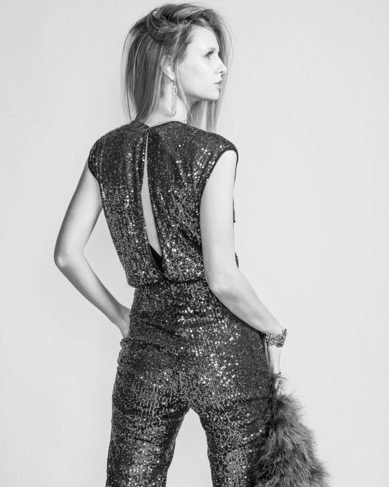 Fashion photography of young woman in stylish sequined jumpsuit standing in fashion pose.