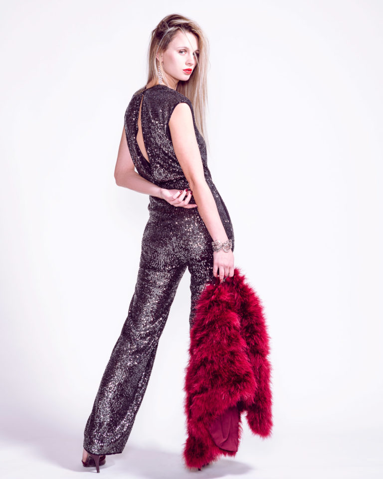 Fashion photography of young woman in stylish sequined jumpsuit standing in fashion pose.